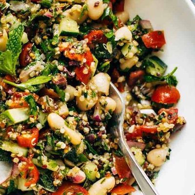 A mixture of quinoa, mint, tomatoes, white beans and radish slices in a bowl.
